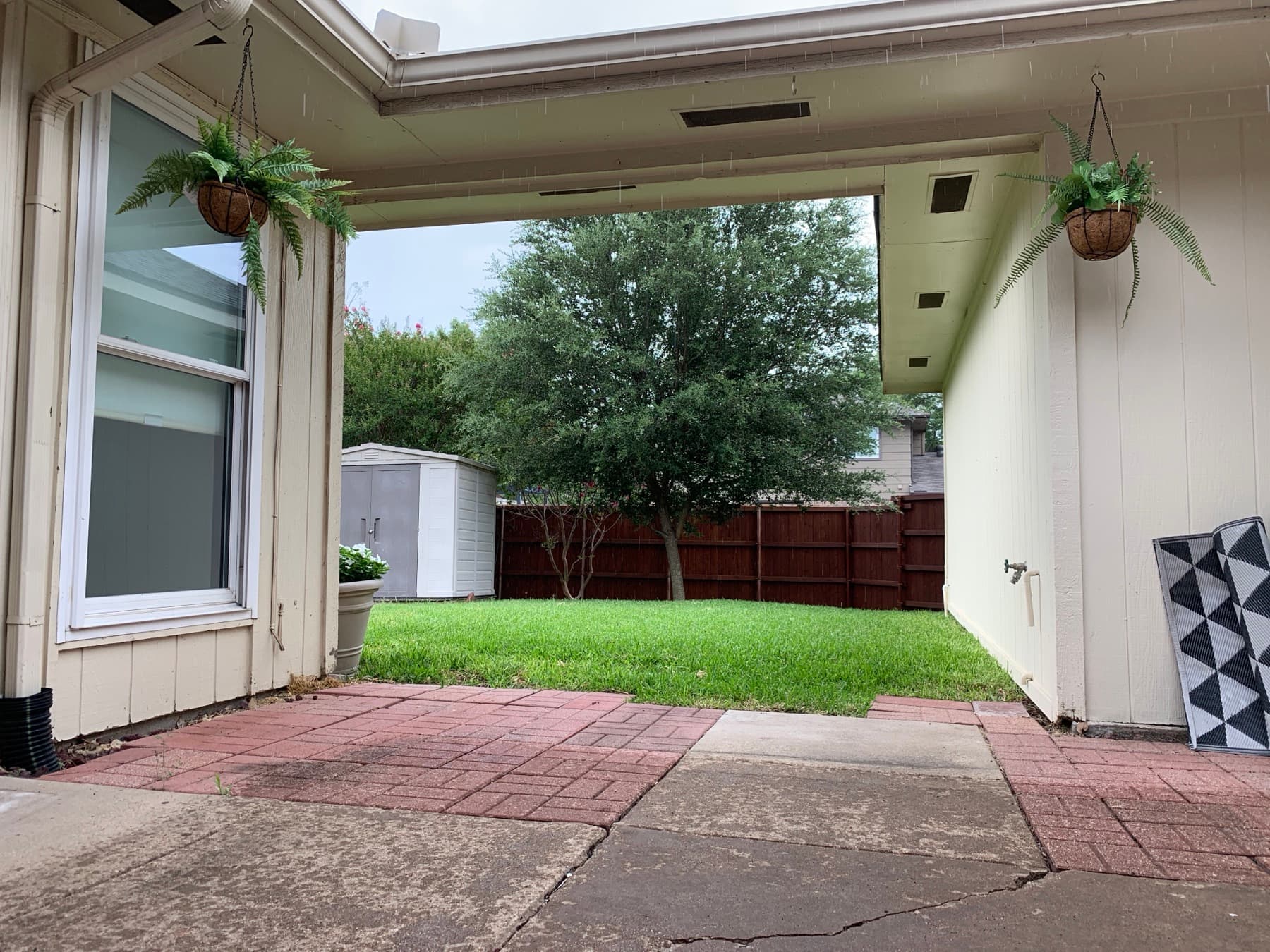 A bare side patio with two hanging ferns