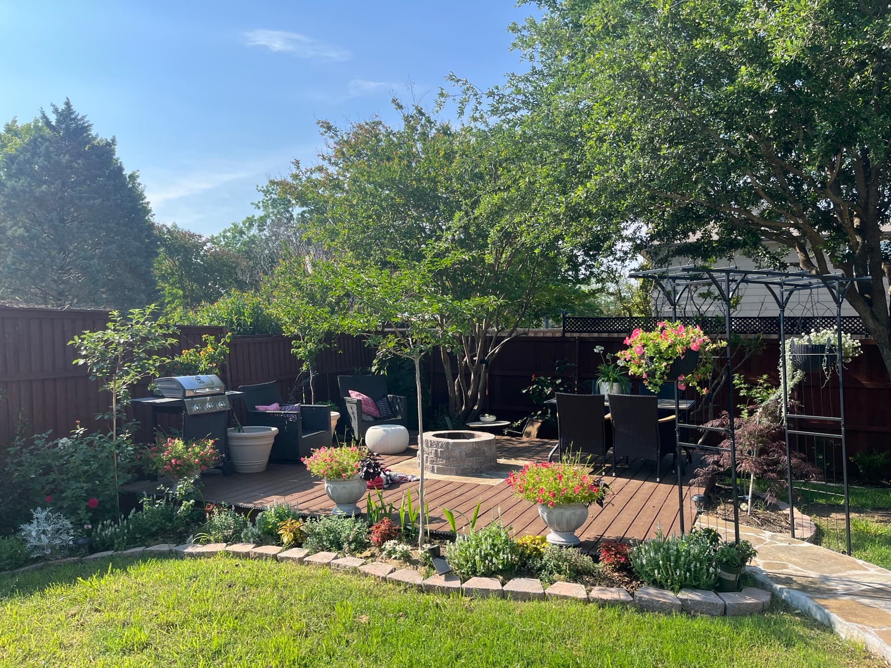 A designed backyard with a deck lounge, fire pit and flagstone path under a bright sky
