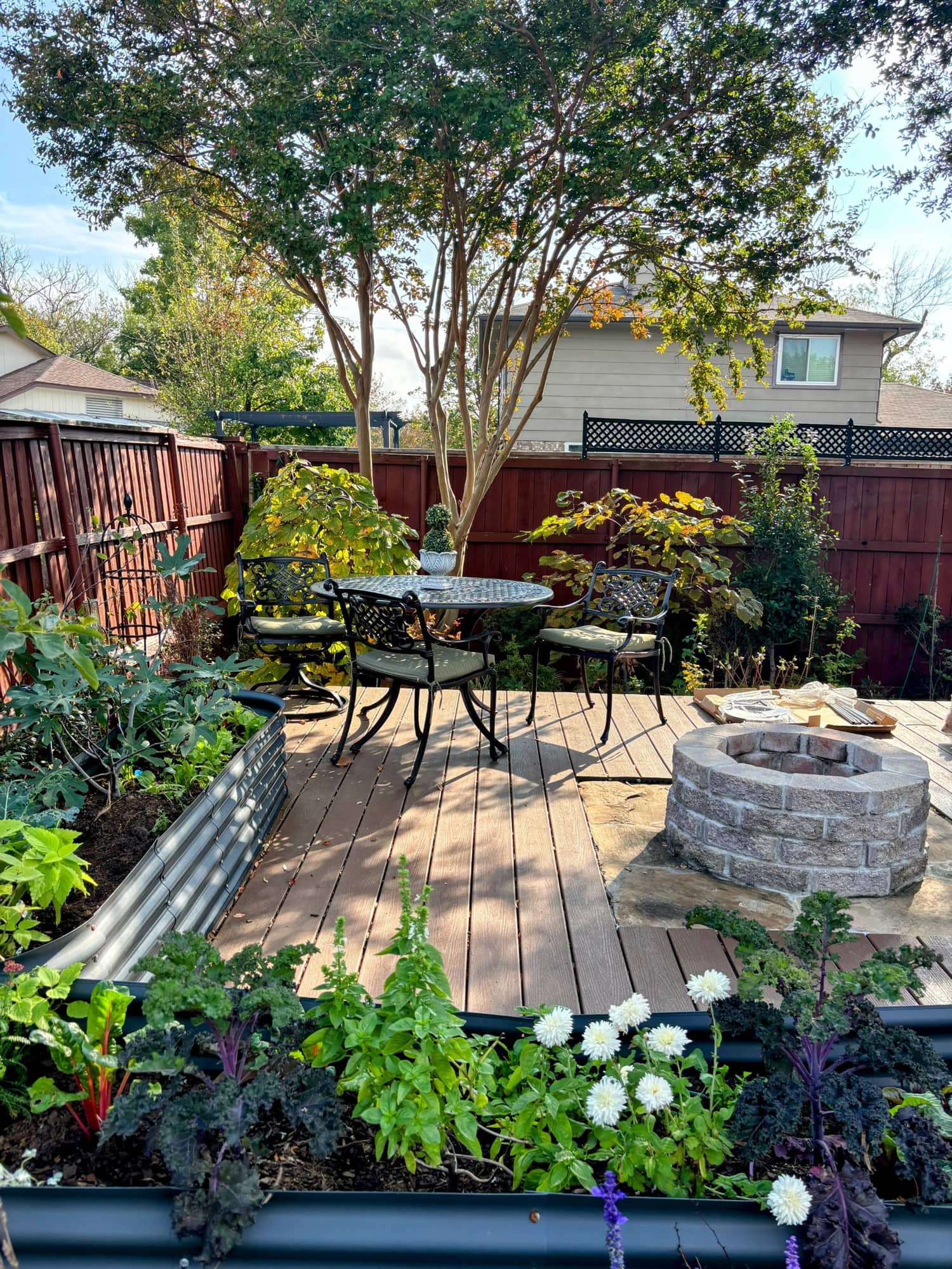 A bistro table and chairs on the garden deck beside the fire pit, under bright trees